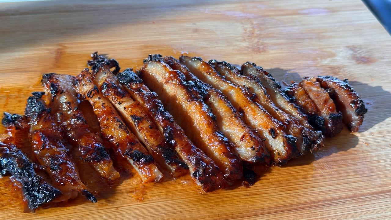 Close-up of sliced glazed BBQ pork on a wooden board